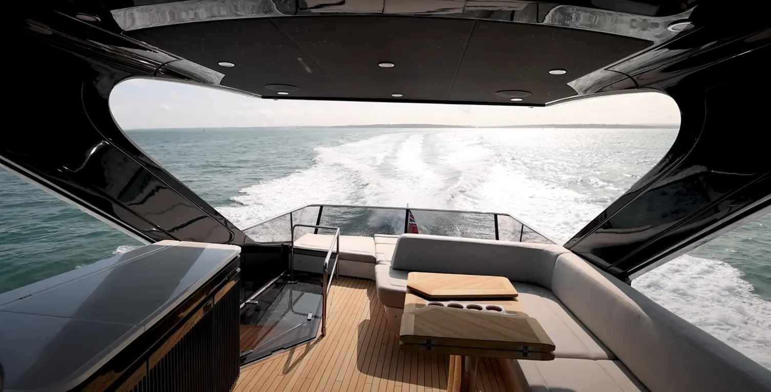 Luxury yacht interior featuring seating and a table, with a view of the sea and wake in the background.